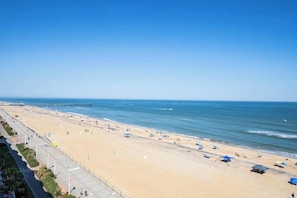 Ein Strand mit einer Seebrücke, blauem Himmel und einem weiten Sandbereich mit Sonnenschirmen.