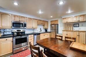 Modern kitchen with central island, equipped with microwave, oven, and dishwasher, featuring light wood cabinetry and dark countertops.