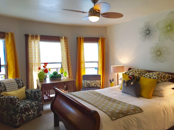 A hotel room with a bed, a desk, a chair, a sofa, and a ceiling fan.