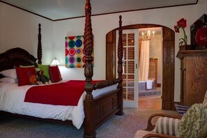 A four-poster bed with a red bedspread and pillows, a wooden headboard, and a colorful abstract painting on the wall. - Distinctive Inns of Kingsville Inn31 (Kingsville)