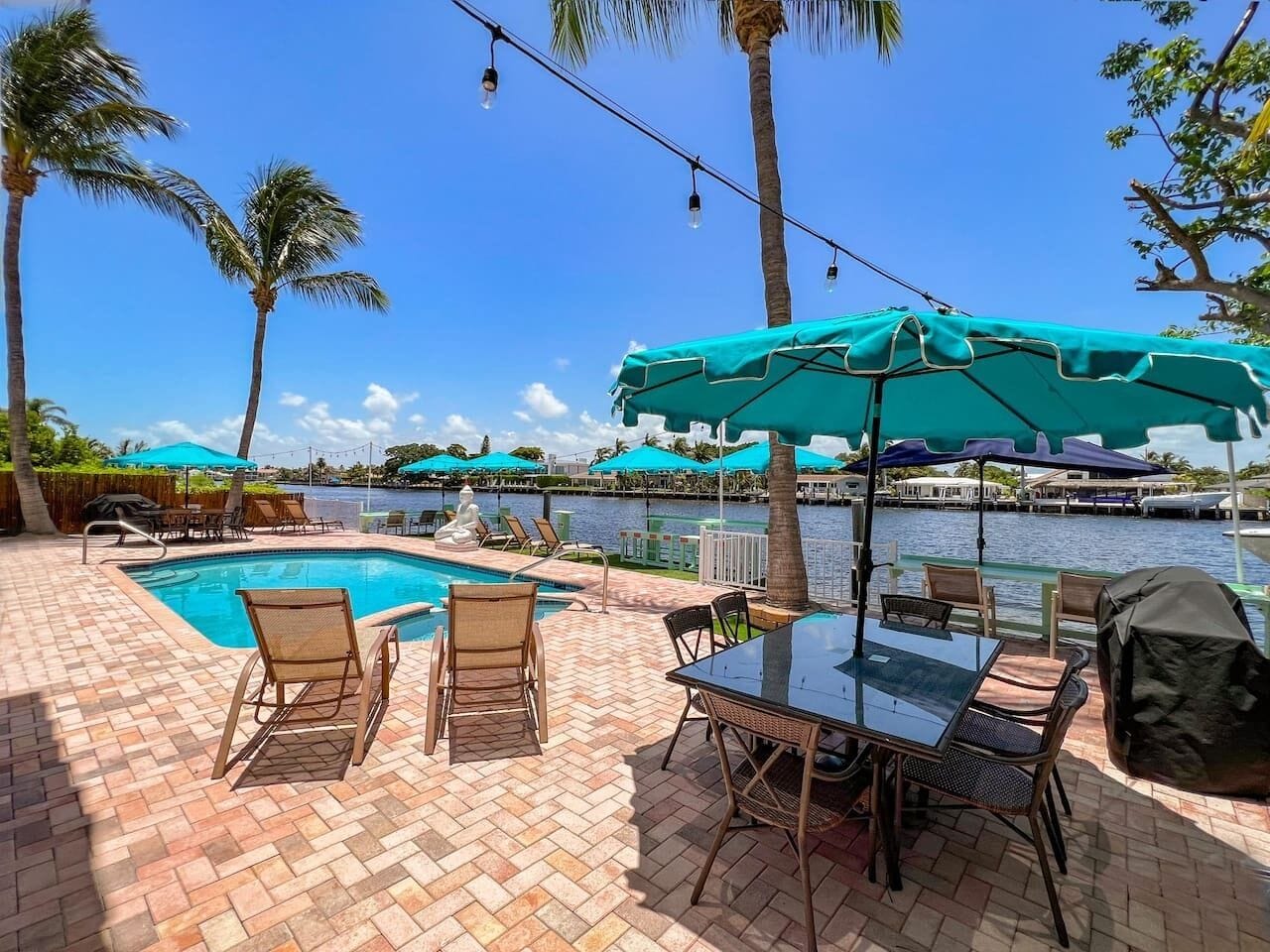 A poolside area with a table and chairs, umbrellas, and a view of the water.