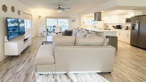 Ein modernes Wohnzimmer mit einem beigefarbenen Ecksofa, einem Flachbildfernseher und einem Essbereich mit Tisch und Stühlen.