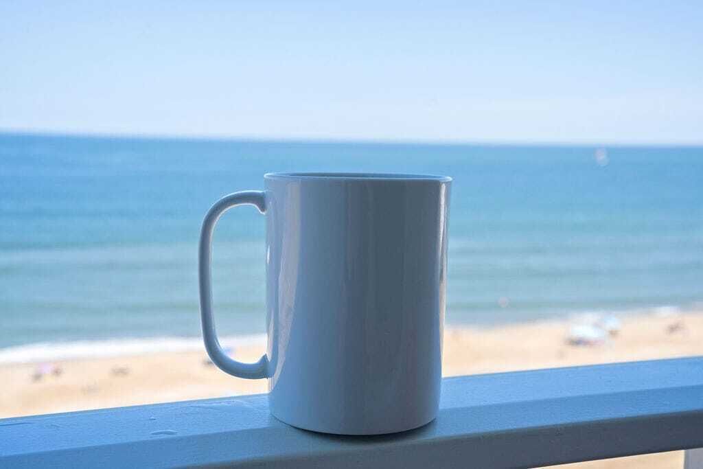 Eine weiße Tasse auf einem Balkon mit Blick aufs Meer.