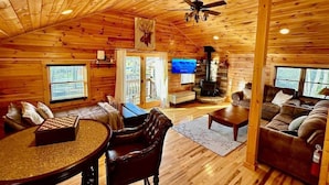 Un interior acogedor de cabaña con paredes de madera, chimenea, televisor y un tablero de ajedrez.