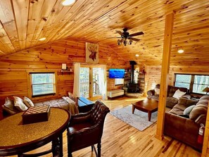 A cozy cabin interior with wooden walls, a fireplace, a television, and a chessboard.