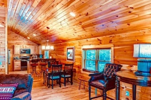 A log cabin interior with a kitchen, dining area, and a large window.