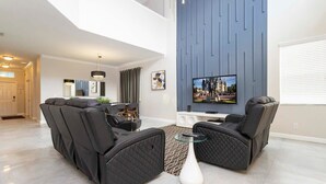 A modern living room with a sectional sofa, a glass coffee table, and a flat-screen TV mounted on a blue accent wall. - Three King Suites & Private Pool! 5BR Near Disney (Kissimmee)