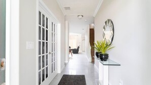 A hallway with a glass console table, a potted plant, and a geometric wall mirror. - Three King Suites & Private Pool! 5BR Near Disney (Kissimmee)