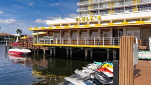 Un hotel frente al agua con un muelle, una lancha rápida y varios jet skis.