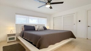 Un dormitorio con una cama, una mesita de noche, una lámpara, un ventilador de techo y una ventana.
