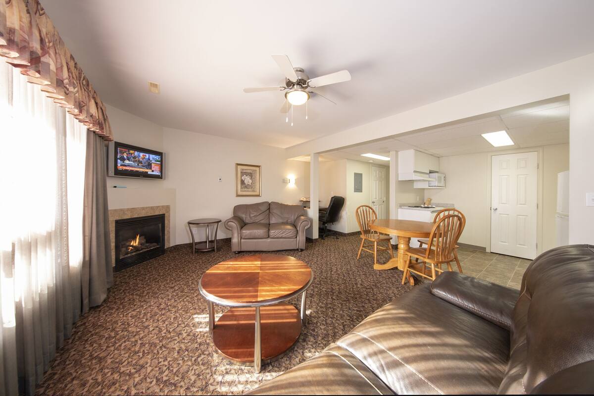 A living room with a fireplace, a sofa, a coffee table, a TV, and a dining area with chairs and a table.