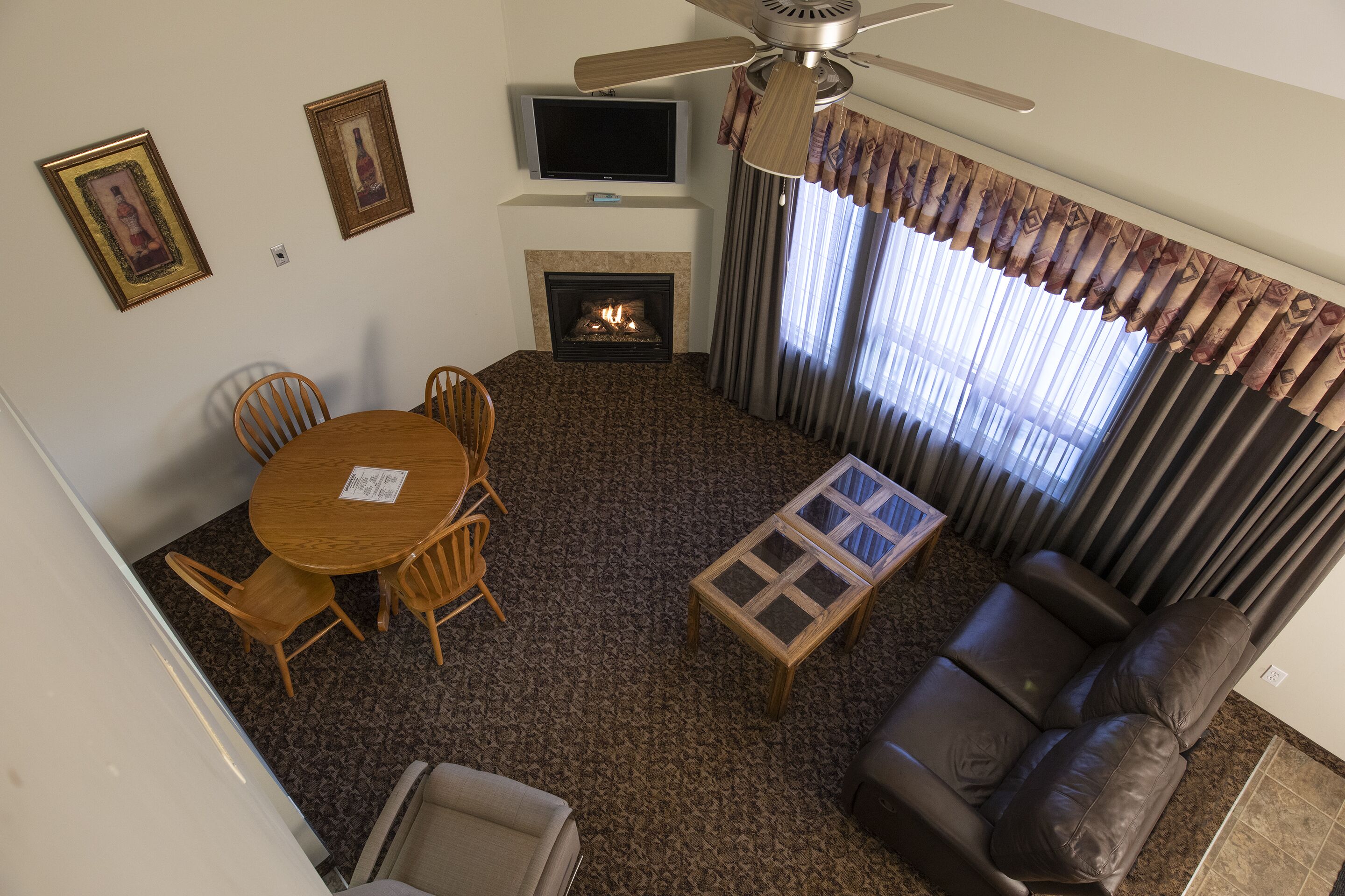Una sala de estar con chimenea, televisor, ventilador de techo, mesa de comedor con sillas y sofá.