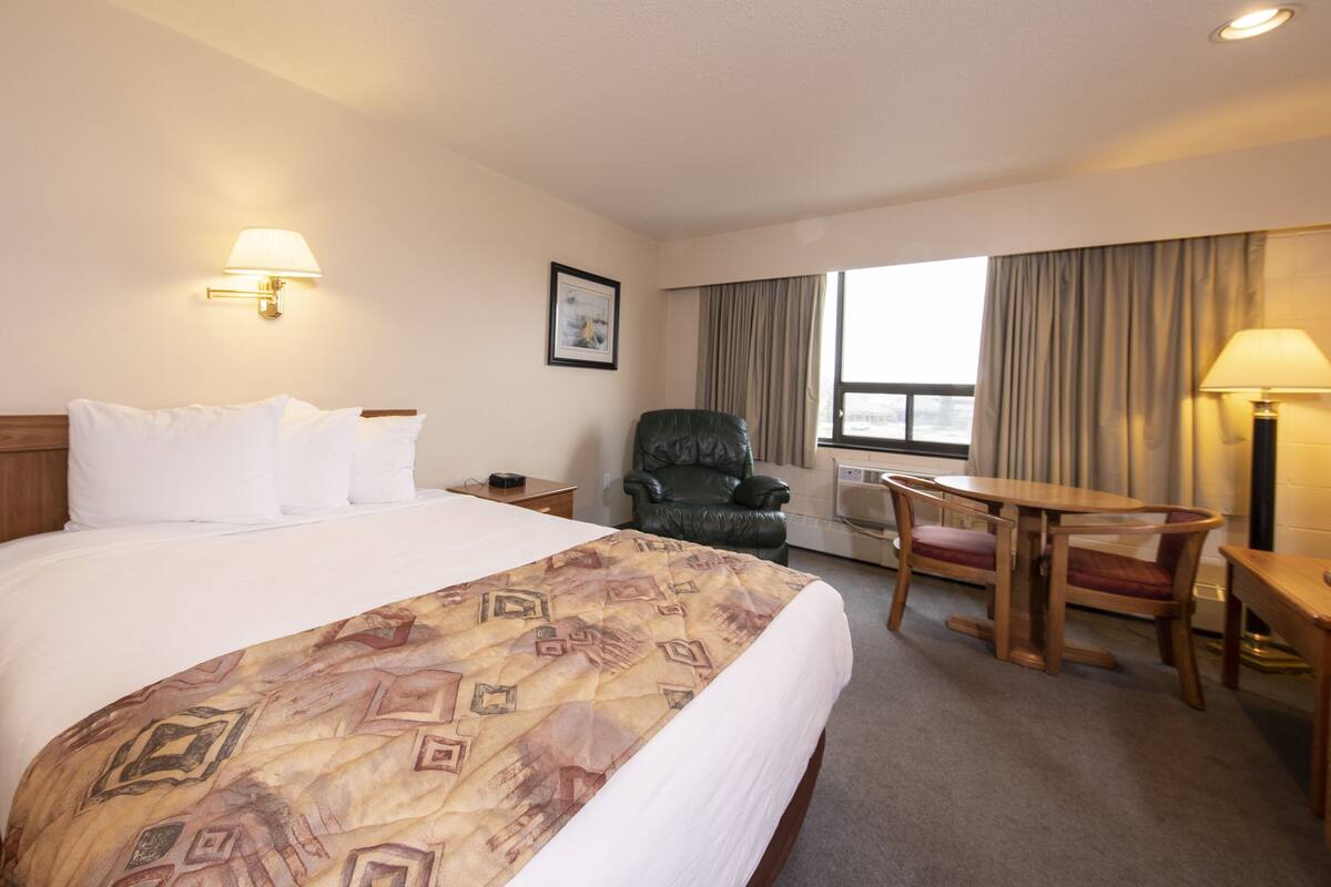 A hotel room with a large bed, a chair, a table, and a window with curtains.