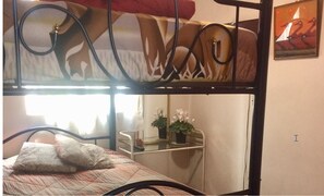 A bunk bed with a patterned mattress, a bedside table with a potted plant, and a window with curtains. - Quito Family And Youth Hostel (Quito)