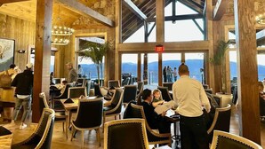 Un restaurant amb bigues de fusta, grans finestres i vista a les muntanyes.