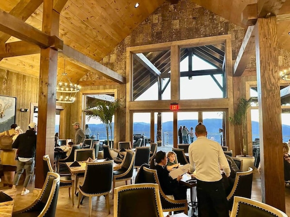 A restaurant with wooden beams, large windows, and a view of the mountains.
