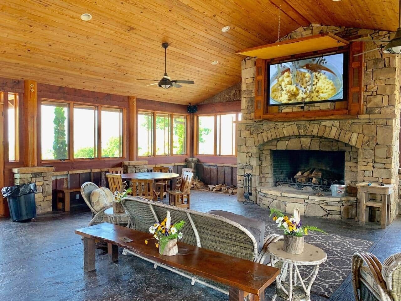 Un vaste espace intérieur doté d’une cheminée en pierre, d’un plafond en bois et de grandes fenêtres.