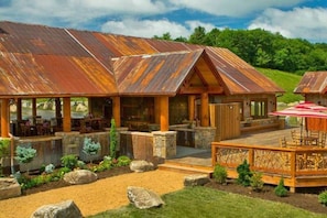 A rustic building with a covered patio area, stone walls, and a grassy landscape.