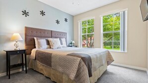A bedroom with a large bed, a nightstand with a lamp, and a window with a view of greenery. - "The Beauty", a SPLENDID Townhome Near Disney - Free WiFi, sleeps 8 comfortably! (Kissimmee)