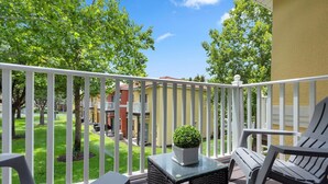 A balcony with white railings, a small table with a potted plant, and two wicker chairs. - "The Beauty", a SPLENDID Townhome Near Disney - Free WiFi, sleeps 8 comfortably! (Kissimmee)