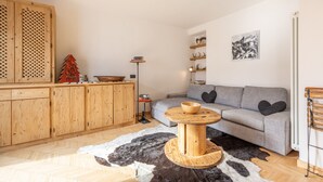 Un salon chaleureux avec un canapé gris, des meubles en bois, une table ronde en bois et un tapis en peau de vache noir et blanc.