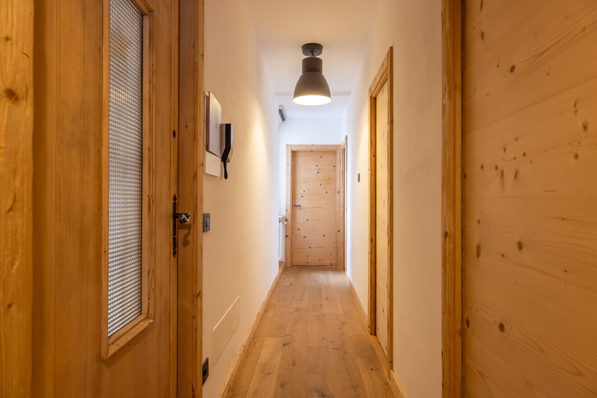 A narrow wooden hallway with a ceiling light, wooden doors, and a wall-mounted telephone.