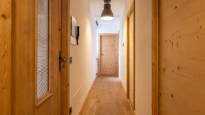 Un couloir étroit en bois, éclairé par un luminaire au plafond, avec des portes en bois et un téléphone fixé au mur.