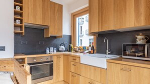 Une cuisine moderne avec des meubles en bois, un four encastré, un four à micro-ondes et une fenêtre donnant sur la rue.