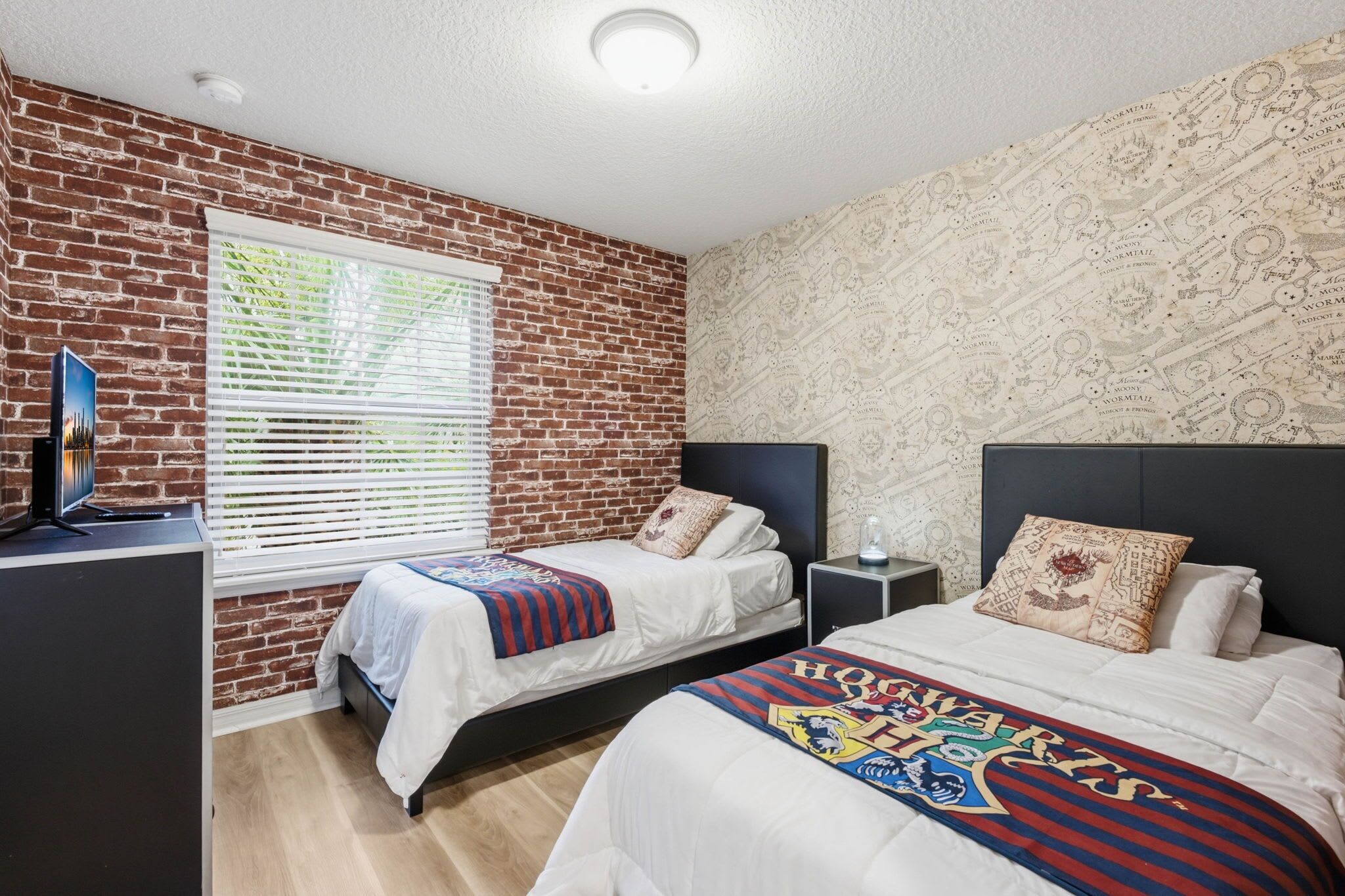 A bedroom with two beds, a TV on a stand, and a brick wall.