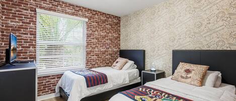 A bedroom with two beds, a TV on a stand, and a brick wall.