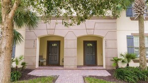 Um edifício com duas portas simétricas, entrada pavimentada e uma pequena área de estar.
