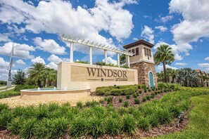 Un letrero que dice 'Windsor at Worldwide' con una pérgola, palmeras y una torre de piedra.