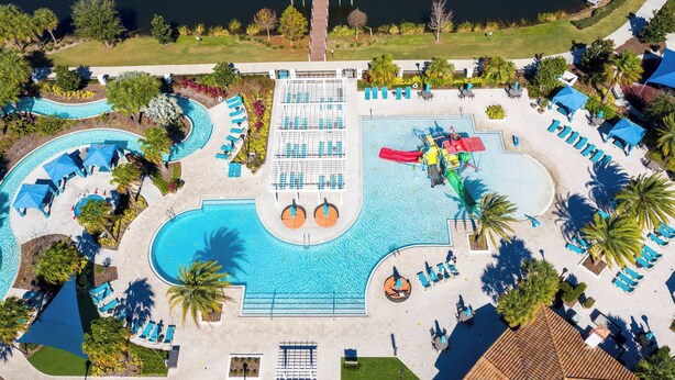 Vista aérea de um resort com uma grande piscina, várias áreas de estar e um píer que leva a um corpo d'água.