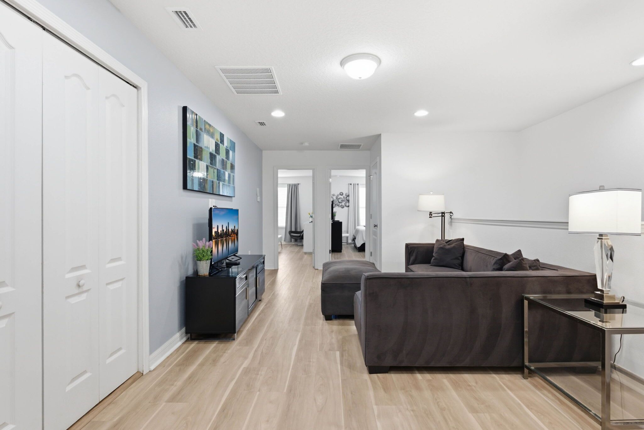 A modern living room with a sofa, a TV, and a lamp. There is a hallway leading to another room.