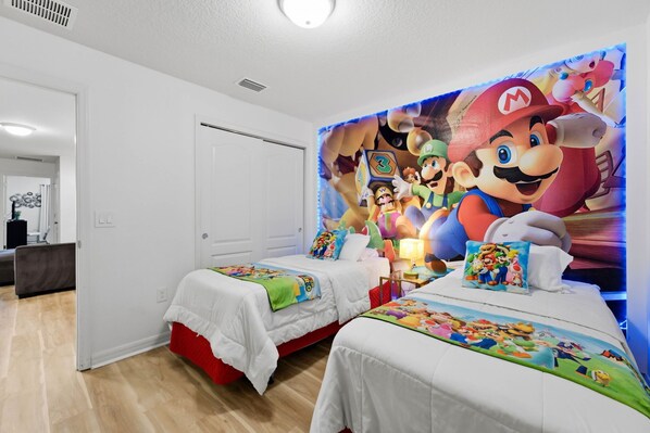 Et soveværelse med to senge, et vægmaleri med Mario-tema og en hvid dør.