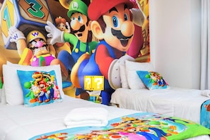 Una habitación de hotel con dos camas, almohadas de colores y un mural de Mario y sus amigos en la pared.