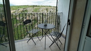 A balcony with a table and chairs, a view of a rocky landscape, and a white wall.