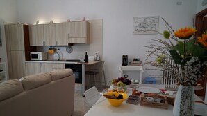 A modern kitchen with wooden cabinets, a dining table with a fruit bowl, and a vase with flowers.