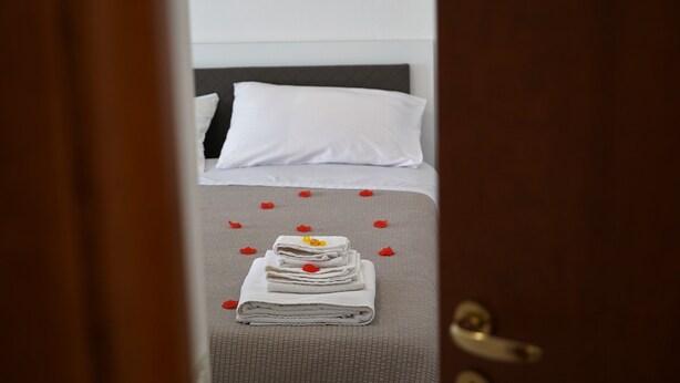 A neatly made bed with white linens and a folded towel at the foot of the bed.