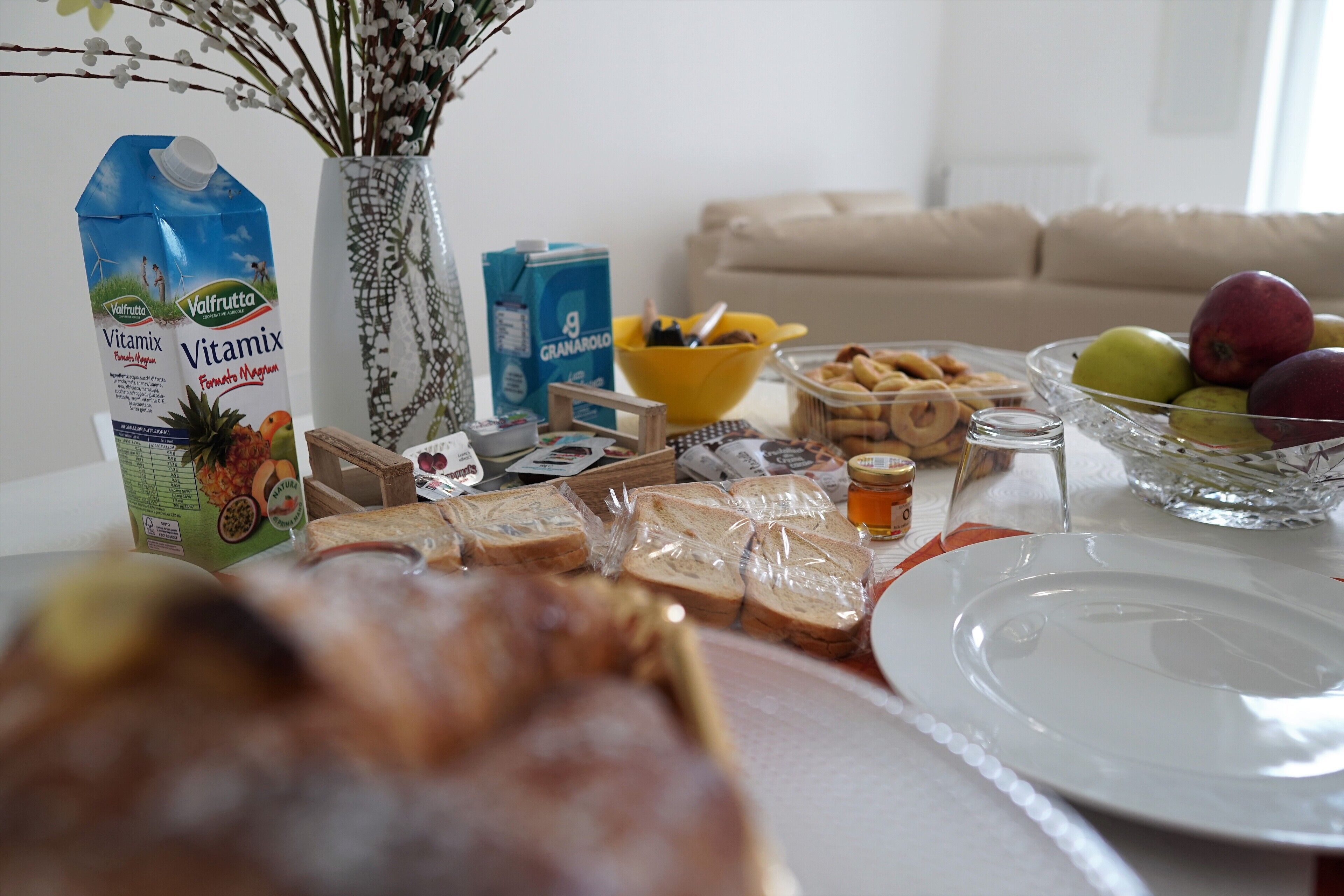 Una mesa de comedor con comida, un florero con flores y un sofá al fondo.