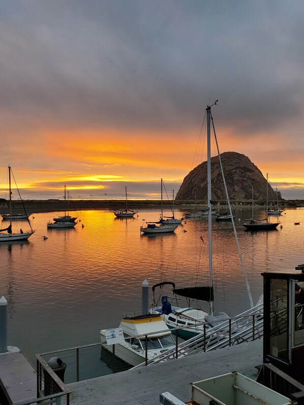 Un puerto deportivo con barcos amarrados, una gran formación rocosa y una puesta de sol.