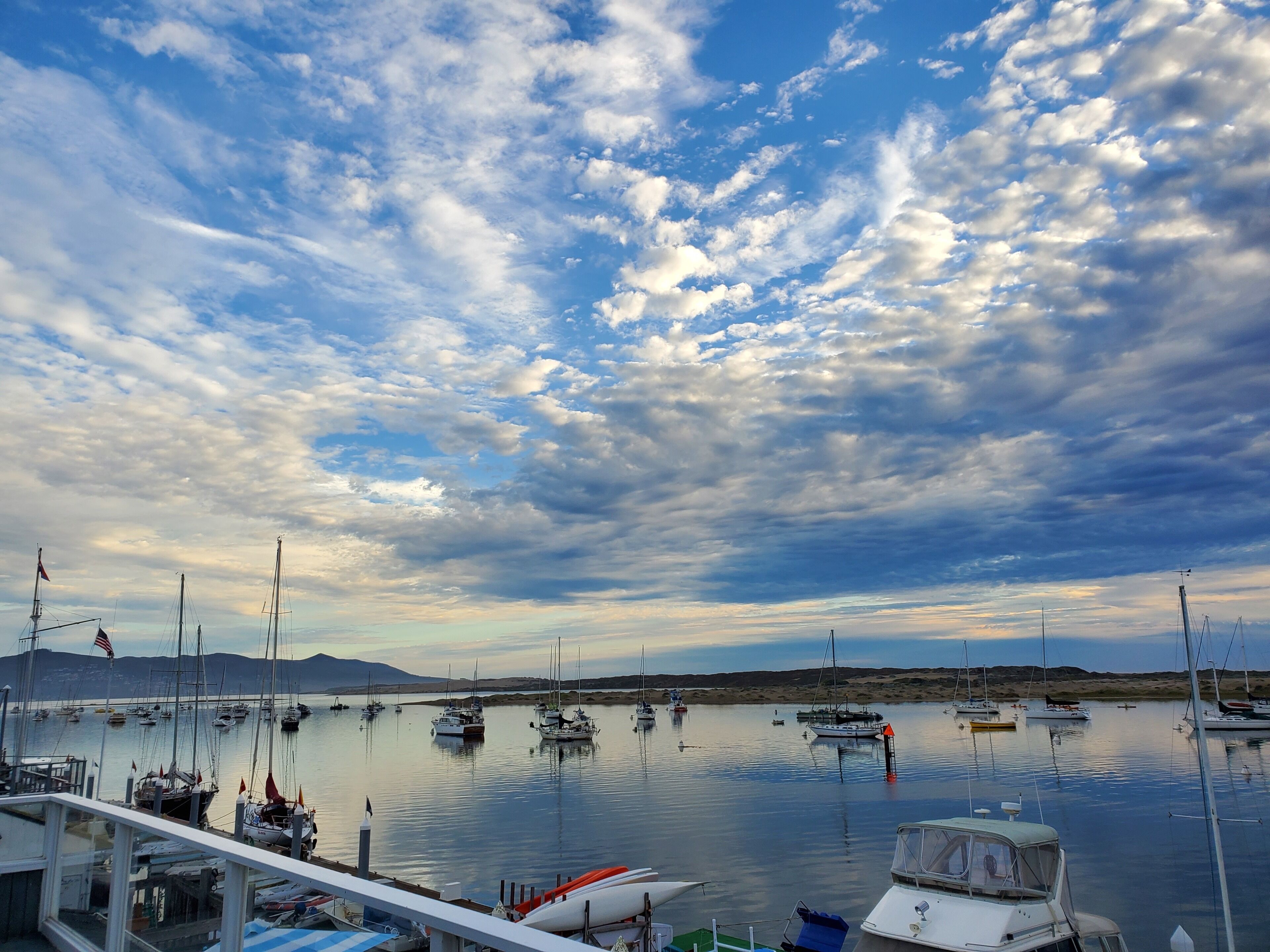 A marina with multiple boats docked, calm water, and a clear sky with clouds.