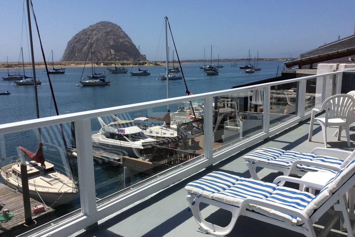 Ein Balkon mit Liegestühlen und Blick auf Boote und eine felsige Insel.