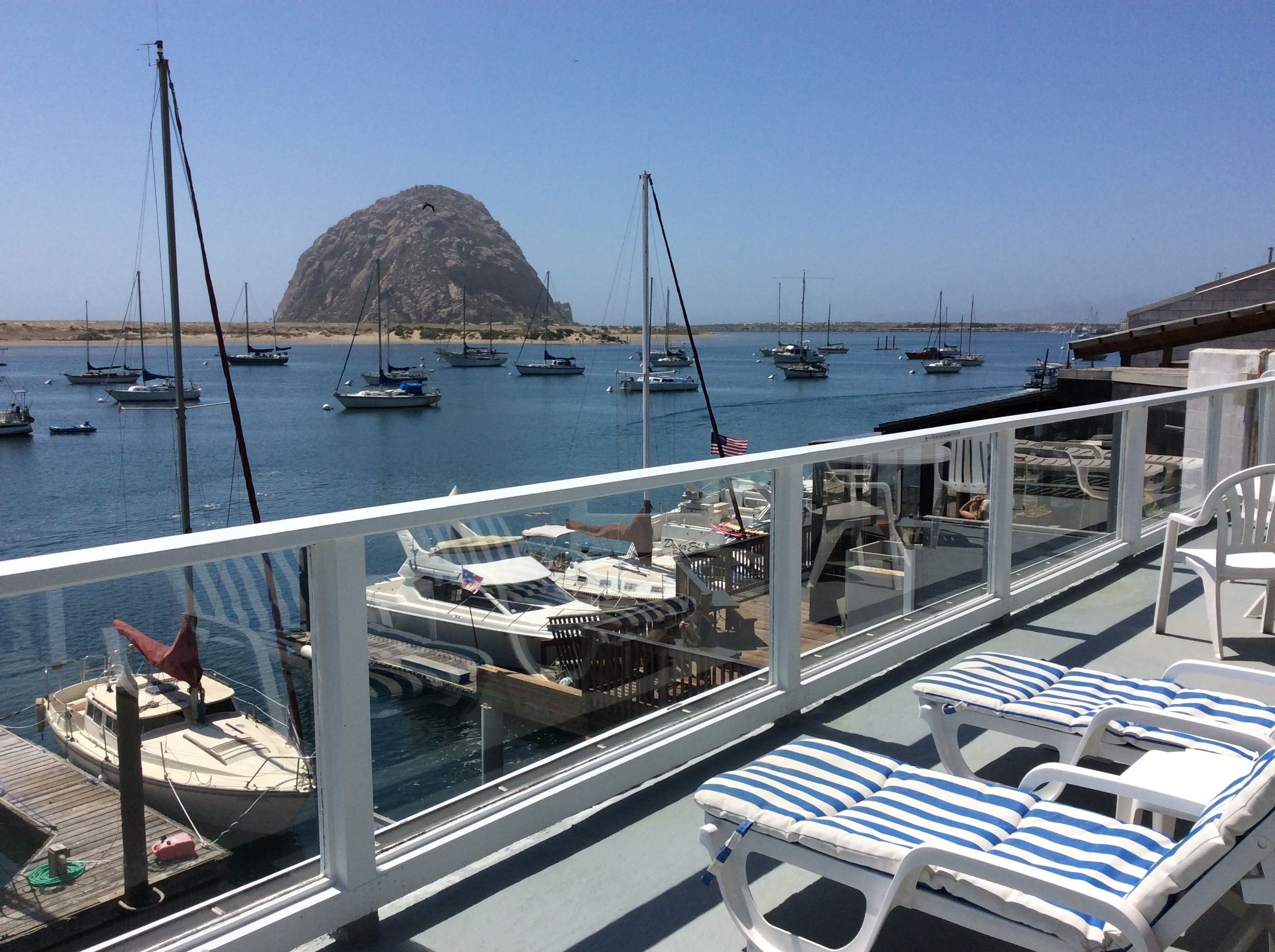Un balcón con sillones blancos y vistas a barcos amarrados en un puerto deportivo.
