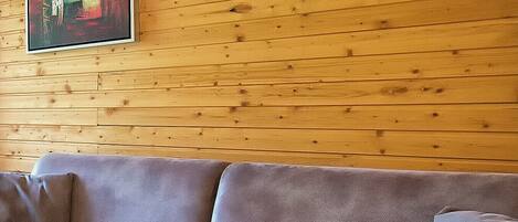 A wooden-paneled wall with a framed artwork and a grey sofa with cushions.