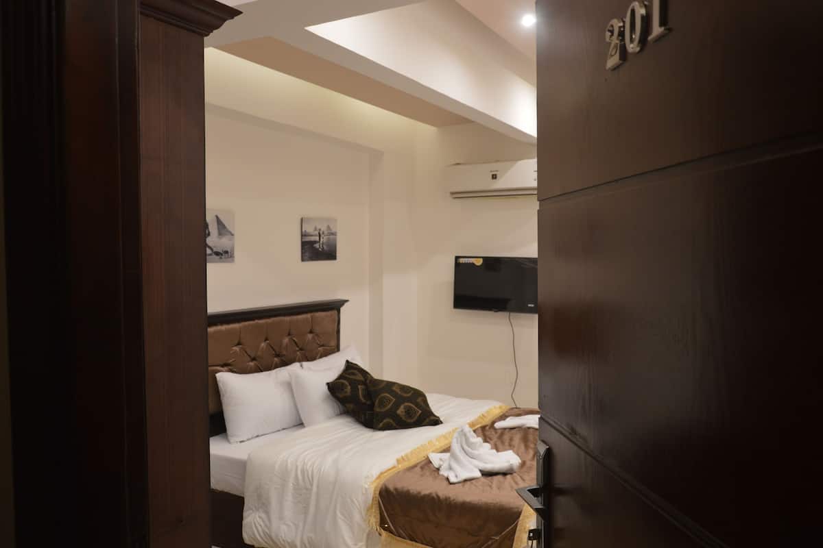 A hotel room with a bed, a flat-screen TV, and a wall-mounted air conditioner.
