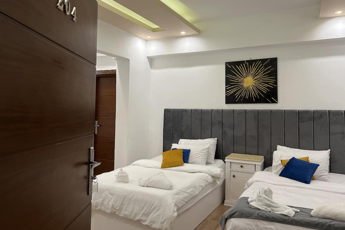 A modern hotel room with two beds, a wooden wardrobe, and a ceiling with recessed lighting.