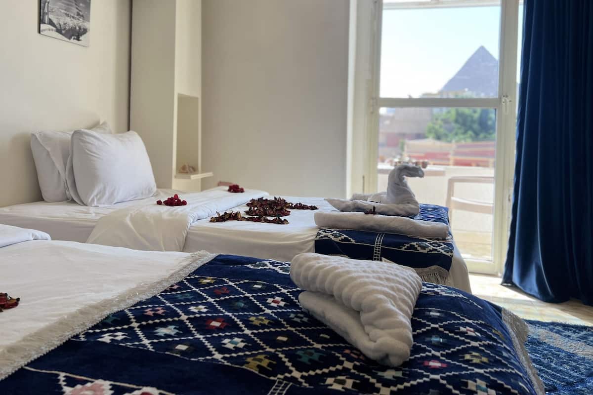 A hotel room with two beds, a patterned rug, and a view of a pyramid through the window.