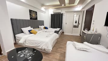 Quarto de hotel com duas camas, uma mesinha, um guarda-roupa e banheiro com espelho e cortina.