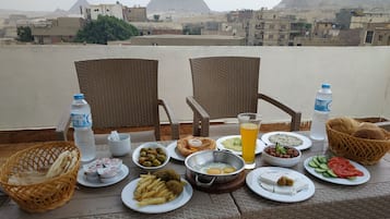 Mesa posta com diversos pratos e bebidas, com vista para um horizonte urbano e pirâmides ao fundo.